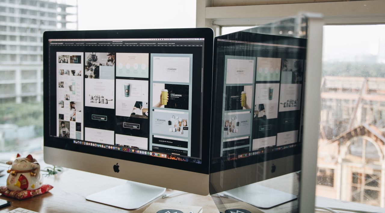 about-us-02 Dual monitors on a desk, showcasing web design in a modern office setting.